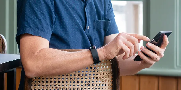 Person using a smartphone with a fitness tracker on their wrist, using the Total Wellbeing Diet app.