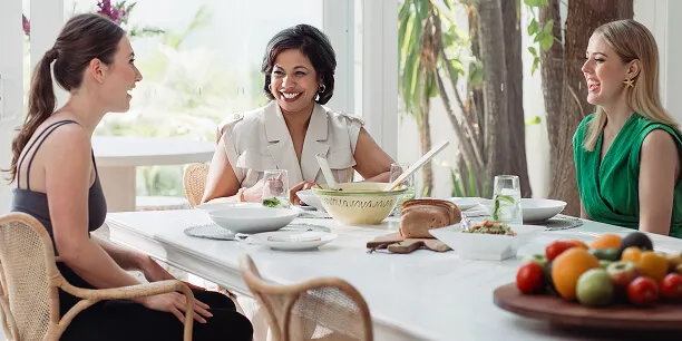 Three female members laughing and enjoying a healthy meal together.